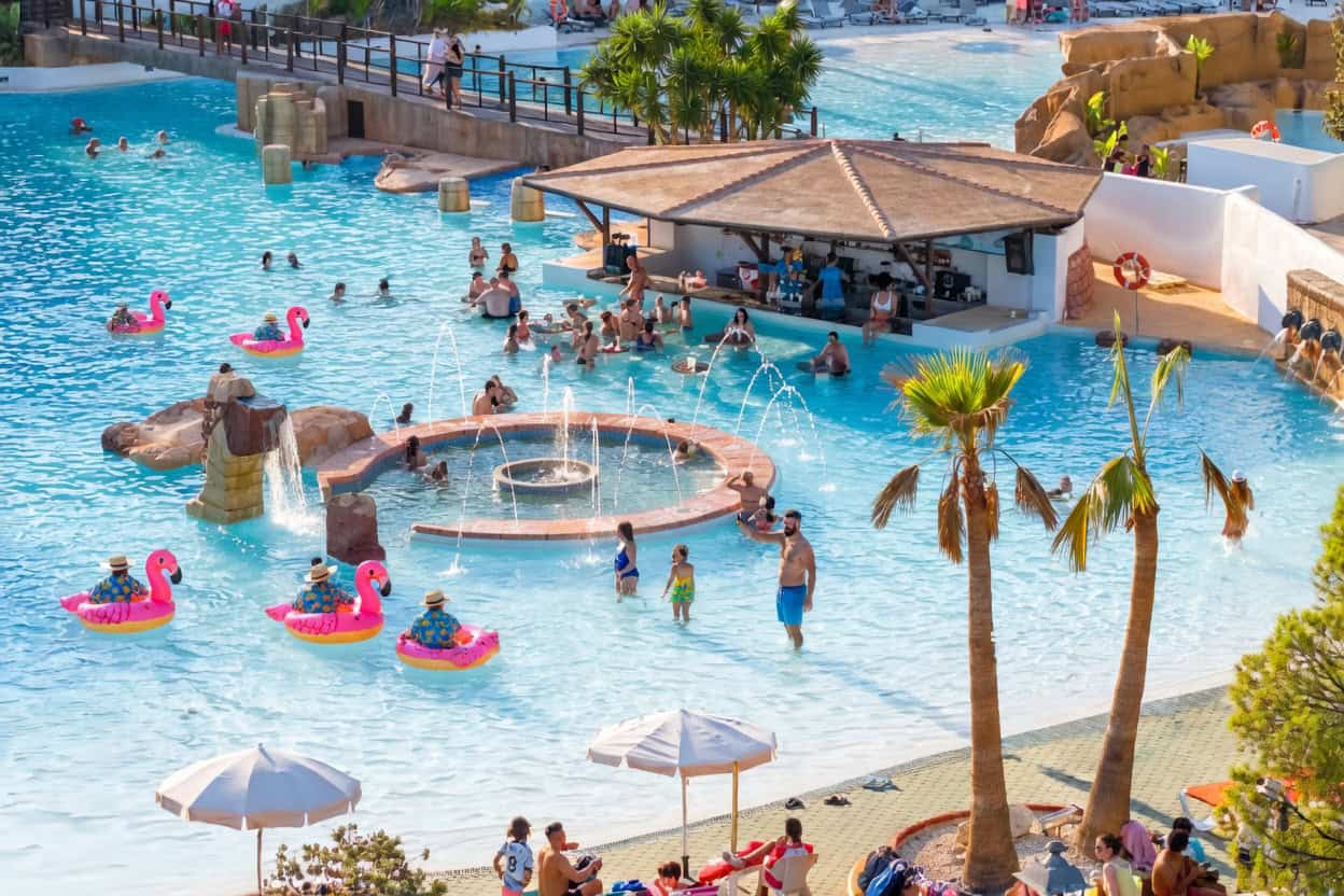 Piscina de hotel con niños y adultos disfrutando del agua y flotadores en un resort de lujo.